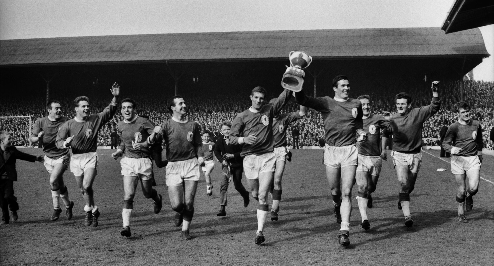 Liverpool players celebrating a league title win at Anfield, with Ron Yeats holding the trophy.